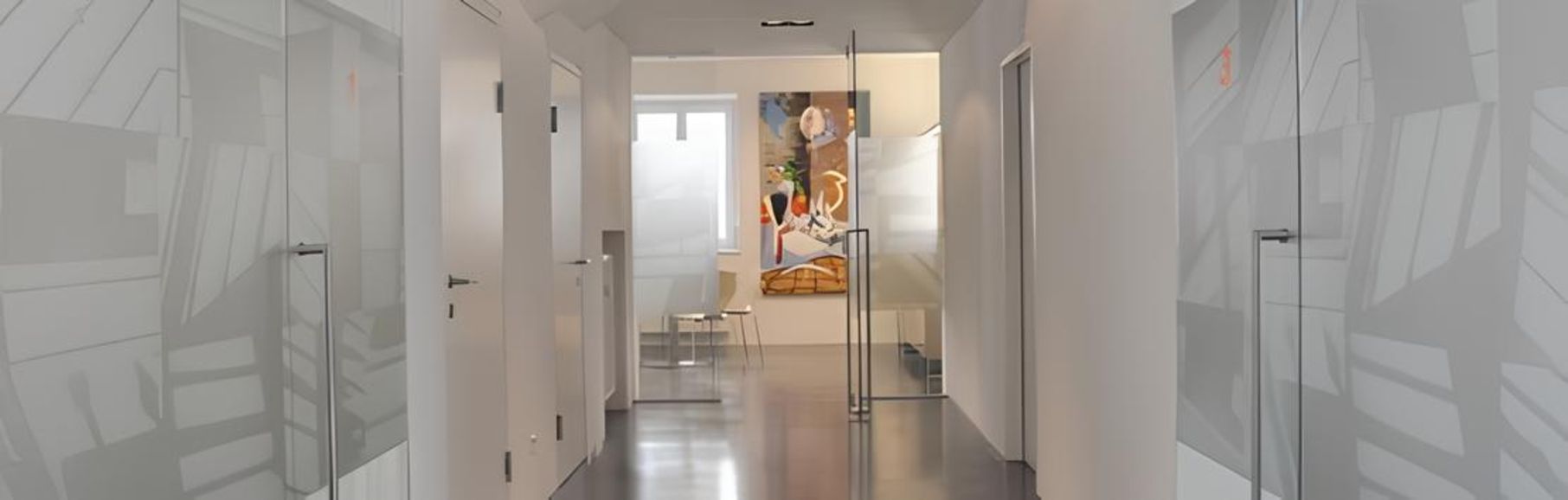 Moderner Büroflur mit Glastüren, weißen Wänden, poliertem Betonboden und einem farbenfrohen Gemälde am Ende.